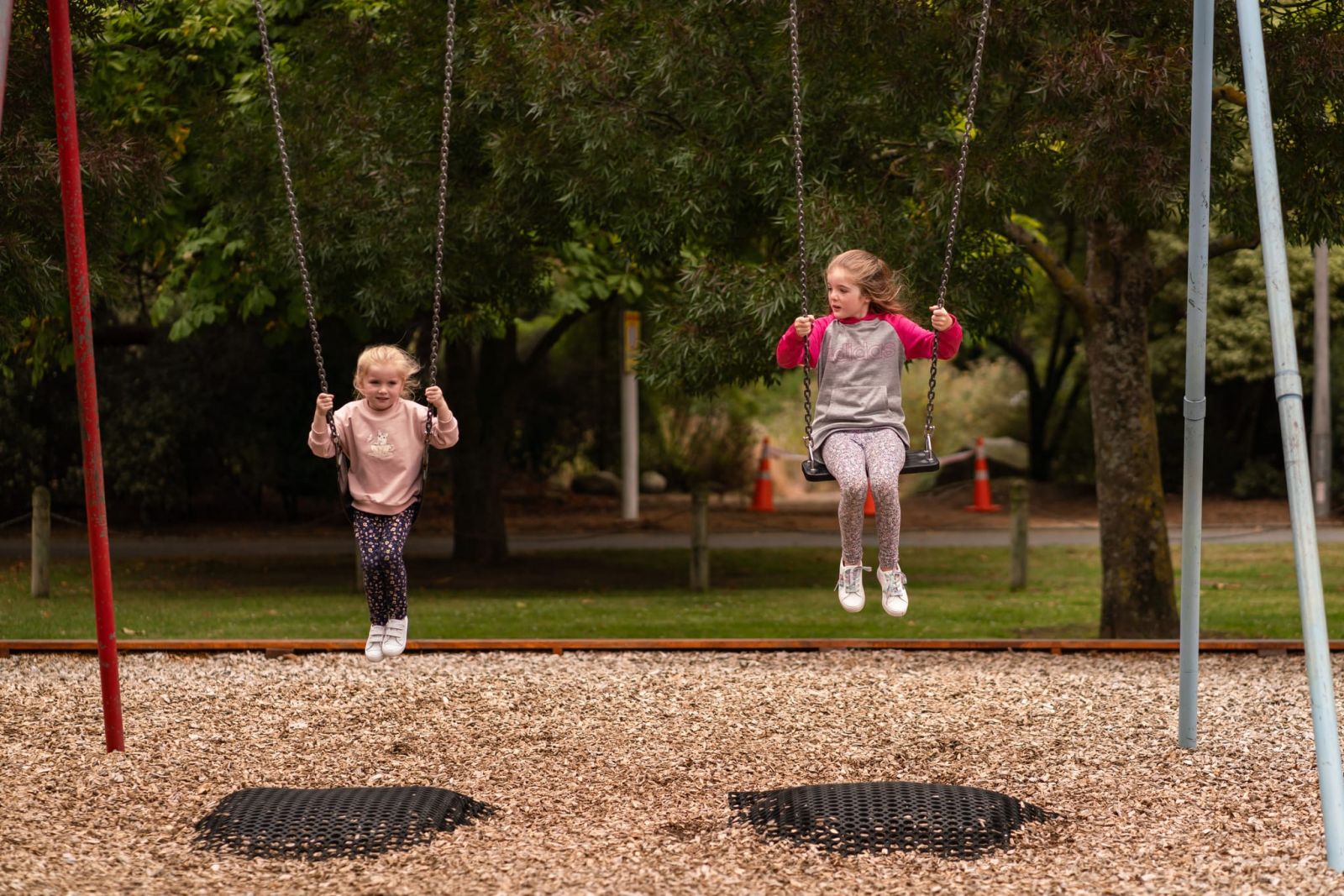 Two girls play at Ashburton domain playground swings banner image